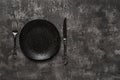 Set table. Black dinner plate, table knife and fork over dark textured surface. Empty porcelain plate near elegant vintage knife