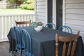 Set table out in the porch of a white home with wooden mismatched chairs Royalty Free Stock Photo