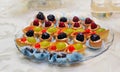 Set of tasty mini cakes with raspberries, blackberries, cranberries, blueberries and grapes on white table. Wedding decoration