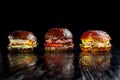 Set of three delicious burgers isolated on a dark background. The concept of fast food, delicious but unwholesome food.