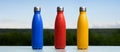 Set of three eco reusable thermo bottles with silver plug, sprayed with water. Blue, red and yellow of color.