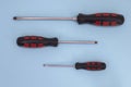 Set of three flat iron screwdrivers with red and black rubber handles. Blue color background. Royalty Free Stock Photo