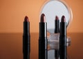 Set of lipsticks on orange reflective surface, one of them reflecting on a cosmetic mirror Royalty Free Stock Photo