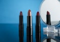 Set of lipsticks on blue reflective surface, one of them reflecting on a cosmetic mirror Royalty Free Stock Photo