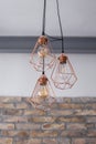 Set of three rose gold light fixtures with black wires in front of a white and brick wall background
