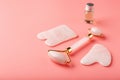 A set of tools for face Massage technique Gua Sha made of natural rose quartz on a pink background. Roller, jade stone and oil in