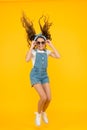 Set a truly energetic and optimistic mood. Energetic little girl with long brunette hair jumping on yellow background