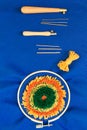 A set of two diassembled punch needles, stranded yellow yarn and embroidered project in a hoop on piece of blue fabric