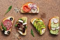 Set of a variety of sandwiches with salmon, sausage, avocado, beet, feta cheese, cucumber and radish on a stone brown background.