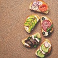 Set of a variety of sandwiches with salmon, sausage, avocado, beet, feta cheese, cucumber and radish on a stone brown background.