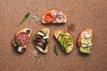 Set of a variety of sandwiches with salmon, sausage, avocado, beet, feta cheese, cucumber and radish on a stone brown background.