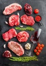 Set of various classic, alternative raw meat steaks with glasses of red wine over black background top view. Big size space for