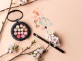 Set of various color eyeshadows for makeup with makeup brush and small white flowers. beige background
