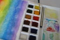 A set of watercolor dry cakes and the brush, a block of watercolor painting rainbow is beside