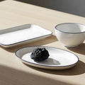 A set of white dishes with blue rims, including a rectangular plate, oval plate with a dark stone, and a bowl, arranged on a light Royalty Free Stock Photo