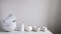 A set of white dishes on the table in the kitchen. Bowls, cups of various shapes, milk jugs, kitchen utensils for tea