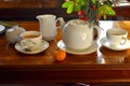 A set of white hot tea pot , teapot, tea cups on mug, milk jar on wooden table and an orange fruit wooden table in afternoon. Trad