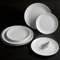 A set of white porcelain plates are displayed on a dark surface, with a small sprig of greenery on one plate Royalty Free Stock Photo