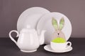 Set of white utensils for lunch and tea party and funny easter bunny on a gray background. Easter set for table service Royalty Free Stock Photo