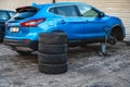 A set of winter tires next to the car in the wheel service, the concept of seasonal tire change