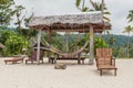 Set of wooden stools and tables for visitors placed under coconut palm trees on the white sands of the beach facing Malet island. Royalty Free Stock Photo