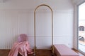 Setting of pink chair with pink bed runner laying on with gold partition rod and white painted wall backgroung