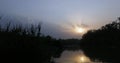 Setting sun behind the clouds over a lake scenic view with plants in foreground Royalty Free Stock Photo