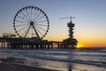 The setting sun has just passed the rear pillar of the Pier in Scheveningen with the ferris wheel and the bungy jump tower