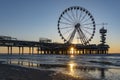 The setting sun is just below the pier in Scheveningen with the ferris wheel and the bungy jump tower, and glistens on the wet san Royalty Free Stock Photo