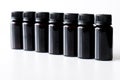 Seven black plastic bottles with lids on a white background. Diagonal. Free space for an inscription. Selective focusing