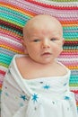 Seven days old baby swaddle with bamboo blankets with stars pattern and a colorful background in a bed