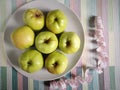 Seven green apples on a flat round plate with a measuring tape serpentine. white double-sided tape measure with inches