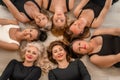 Seven happy women lie on their backs on the floor with their heads pressed together.