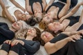 Seven happy women lie on their backs on the floor with their heads together on the floor. Six women are dressed in