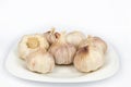 Seven heads of young garlic on a white plate. Close-up. White background