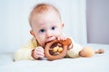 A seven-month-old girl with blue eyes lies on her stomach in a bright room and nibbles a wooden toy, looks at the camera the child Royalty Free Stock Photo