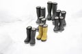 Seven pair of winter rubber boots different sizes standing on snow, one pair is yellow. Seasonal shoes for all family, adult and