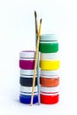 seven plastic jars of gouache for drawing stacked pyramid on a white background, standing next to the brush