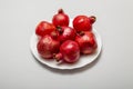 Seven ripe red pomegranates on a white plate on a gray background
