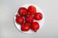 Seven ripe red pomegranates on a white plate on a gray background, top view