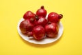 Seven ripe red pomegranates on a white plate on a yellow background