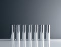Seven sleek, chromed cylinders stand upright on a reflective white surface against a gradient gray background. Royalty Free Stock Photo