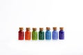 Seven tiny glass bottles with a cork stopper, filled with a rainbow colours of beads, on a white background Royalty Free Stock Photo