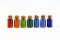 Seven tiny glass bottles with a cork stopper, filled with a rainbow colours of beads, on a white background Royalty Free Stock Photo