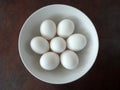 Seven White Eggs in a White Bowl against a Brown Background