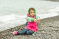 Seven-year girl sitting on a pebble beach in warm clothing and pours out through her fingers small stones
