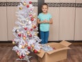 Seven-year girl stands in a box with Christmas toys and Christmas tree Royalty Free Stock Photo