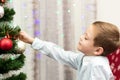 A seven-year-old boy in a blue shirt decorates a Christmas tree with toys on New Year`s Eve at home against a background of garla Royalty Free Stock Photo