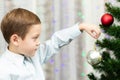 A seven-year-old boy in a blue shirt decorates a Christmas tree with toys on New Year`s Eve at home against a background of garla Royalty Free Stock Photo