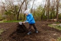 Seven-year-old boy in a blue windbreaker and hat digging humus sapper shovel in the garden